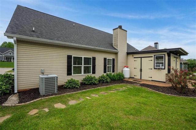 rear view of property with cooling unit, a lawn, a shingled roof, and a chimney