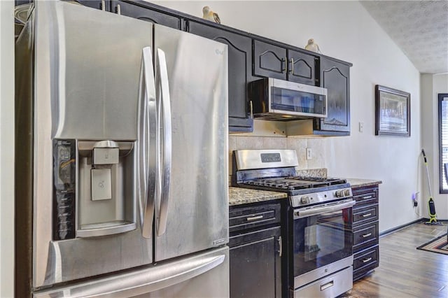 kitchen featuring tasteful backsplash, light stone countertops, stainless steel appliances, a textured ceiling, and dark wood-style flooring