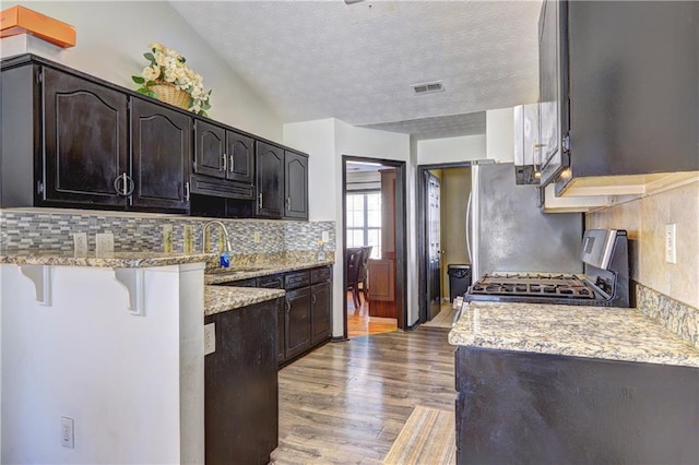 kitchen with visible vents, a kitchen bar, light wood-style flooring, a sink, and range with gas stovetop