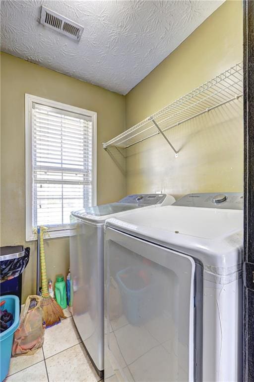 clothes washing area featuring visible vents, laundry area, tile patterned floors, washer and dryer, and a textured ceiling