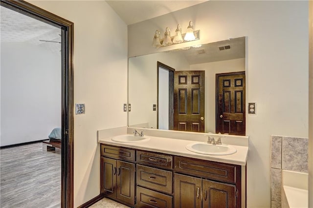 ensuite bathroom with a sink, visible vents, baseboards, and double vanity