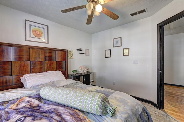 bedroom with baseboards, visible vents, light wood finished floors, ceiling fan, and a textured ceiling