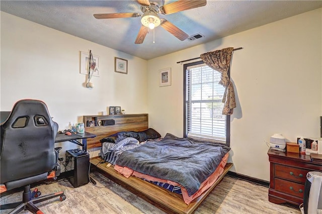 bedroom with ceiling fan, wood finished floors, visible vents, and a textured ceiling