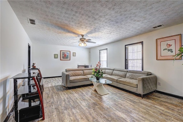 living room with a textured ceiling, wood finished floors, visible vents, and baseboards