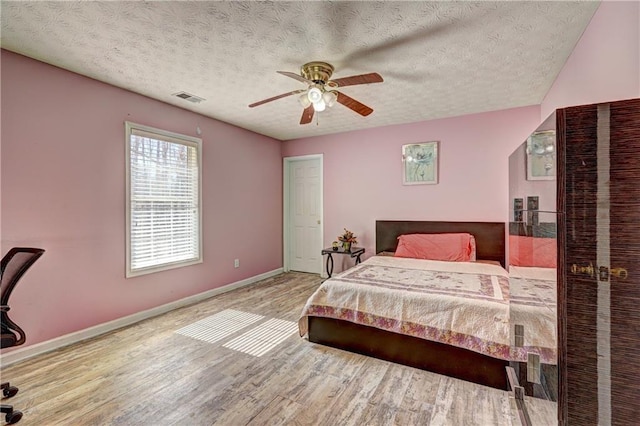 bedroom with visible vents, baseboards, a textured ceiling, and wood finished floors