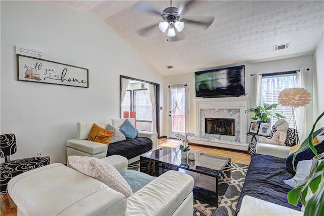 living room featuring visible vents, a textured ceiling, wood finished floors, a fireplace, and vaulted ceiling