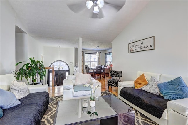 living area featuring ceiling fan with notable chandelier, wood finished floors, and vaulted ceiling