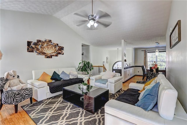 living area with ceiling fan, a textured ceiling, lofted ceiling, and wood finished floors