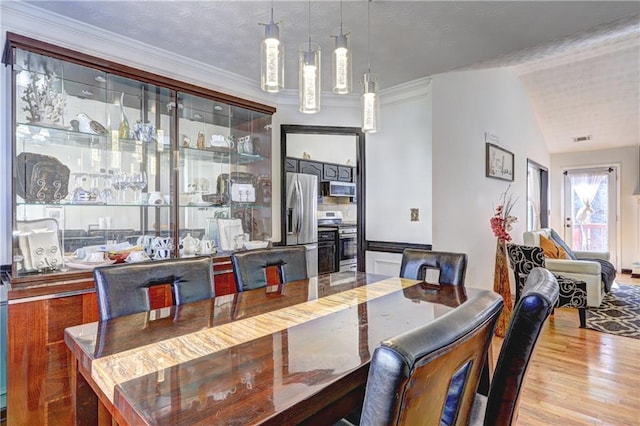 dining space featuring visible vents, lofted ceiling, ornamental molding, wood finished floors, and a textured ceiling