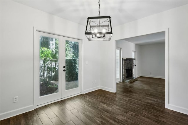 unfurnished dining area with a stone fireplace, dark wood-type flooring, french doors, and a chandelier