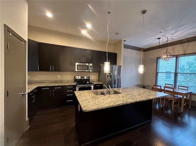 kitchen featuring dark wood-style flooring, a kitchen island with sink, a sink, appliances with stainless steel finishes, and pendant lighting