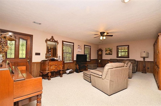 carpeted living room with wooden walls, ceiling fan, and a textured ceiling