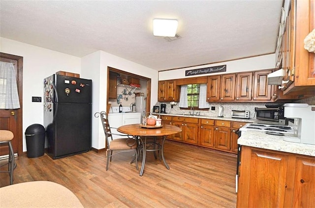 kitchen with range, washer and clothes dryer, black refrigerator, and light hardwood / wood-style flooring