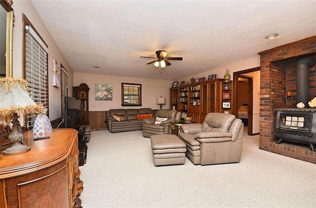 carpeted living room with a wood stove, ceiling fan, and a textured ceiling