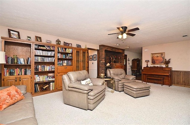 carpeted living room with ceiling fan, wood walls, and a textured ceiling