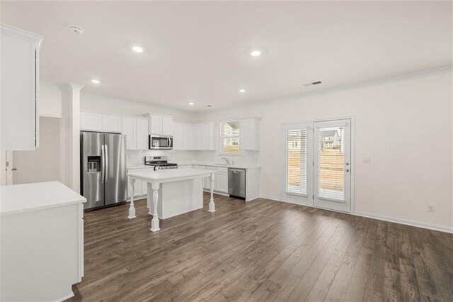 kitchen with a kitchen island, a kitchen breakfast bar, appliances with stainless steel finishes, white cabinets, and ornamental molding