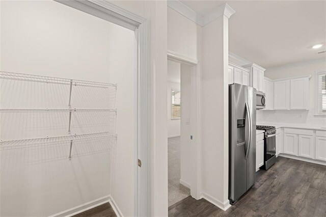 kitchen with white cabinets, ornamental molding, stainless steel appliances, and dark wood-type flooring