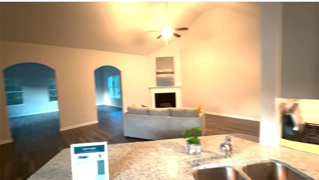 kitchen with a sink, a fireplace, baseboards, ceiling fan, and arched walkways