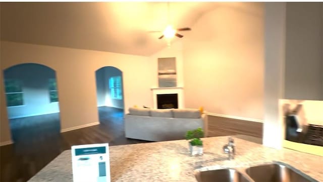 kitchen with a sink, a fireplace, baseboards, ceiling fan, and arched walkways