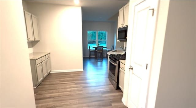kitchen with stainless steel gas range, light countertops, baseboards, and light wood-style floors