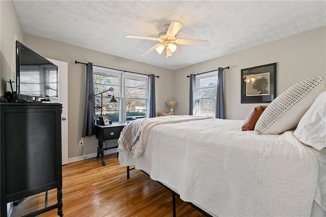 bedroom with baseboards, ceiling fan, light wood-style flooring, and a textured ceiling