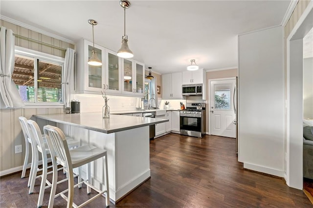 kitchen featuring dark wood finished floors, appliances with stainless steel finishes, glass insert cabinets, white cabinetry, and a peninsula