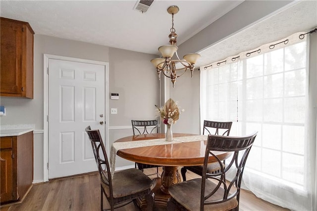 dining space featuring light wood finished floors, visible vents, a chandelier, and baseboards