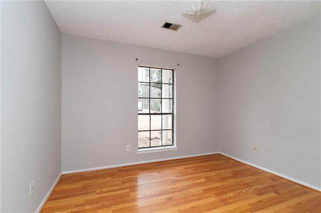 spare room featuring visible vents, baseboards, light wood-style floors, and a textured ceiling