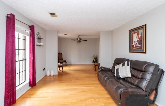 living room featuring a textured ceiling, light wood-style floors, visible vents, and ceiling fan