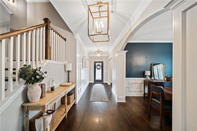 entrance foyer with decorative columns, crown molding, dark wood-type flooring, and a chandelier