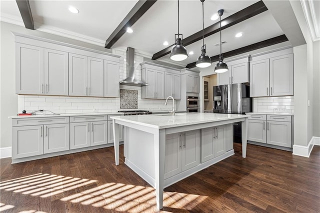 kitchen featuring appliances with stainless steel finishes, wall chimney exhaust hood, a breakfast bar, hanging light fixtures, and an island with sink