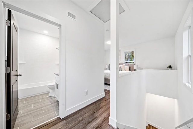 hall featuring visible vents, attic access, baseboards, and wood finished floors