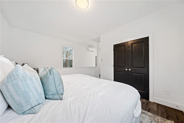 bedroom with baseboards, an AC wall unit, and wood finished floors