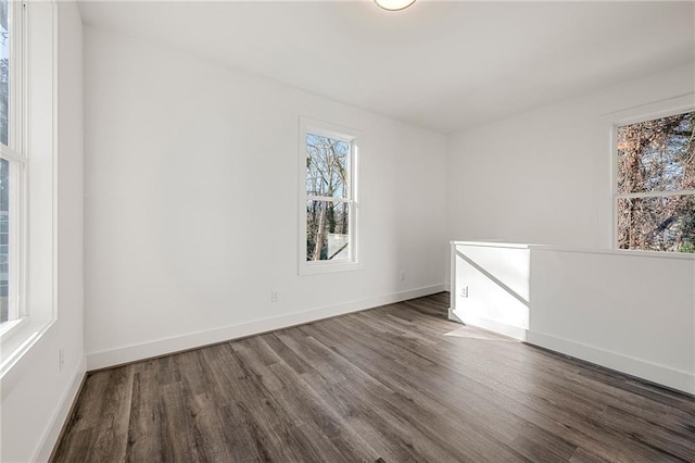 empty room featuring baseboards, plenty of natural light, and dark wood-style flooring