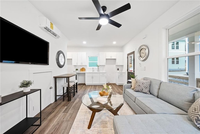 living room featuring a wall unit AC, recessed lighting, light wood finished floors, and ceiling fan