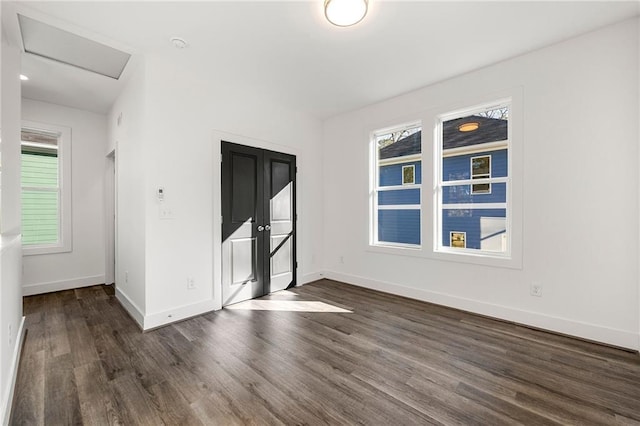 spare room featuring dark wood finished floors, attic access, and baseboards