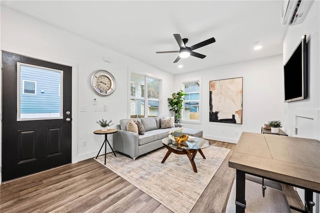 living room featuring baseboards, a wall mounted AC, a ceiling fan, and wood finished floors