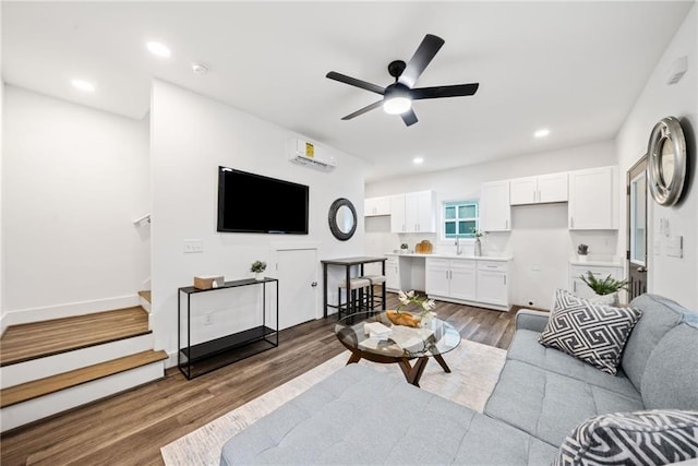 living area with a wall unit AC, wood finished floors, a ceiling fan, recessed lighting, and stairs