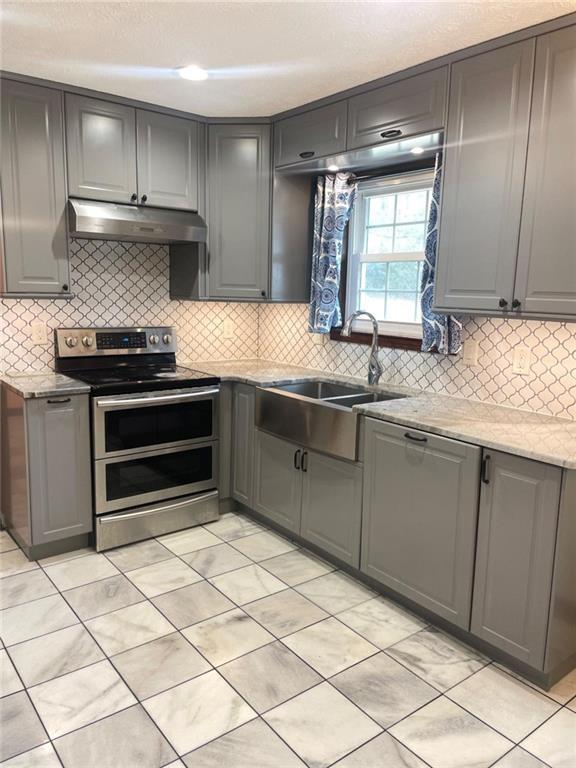 kitchen featuring gray cabinetry, sink, light stone countertops, and range with two ovens