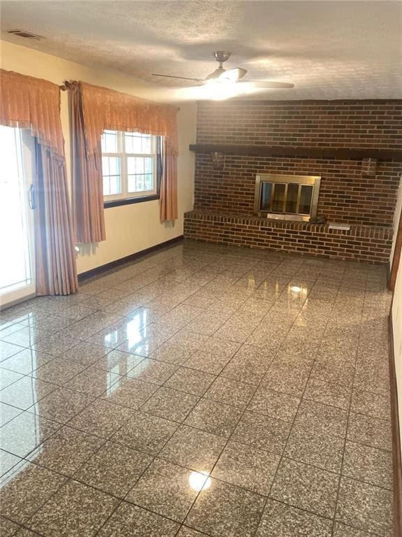 empty room featuring ceiling fan, a fireplace, a textured ceiling, and brick wall