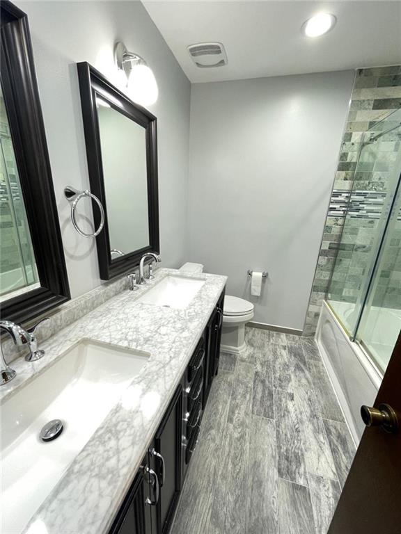 full bathroom with bath / shower combo with glass door, hardwood / wood-style floors, vanity, and toilet