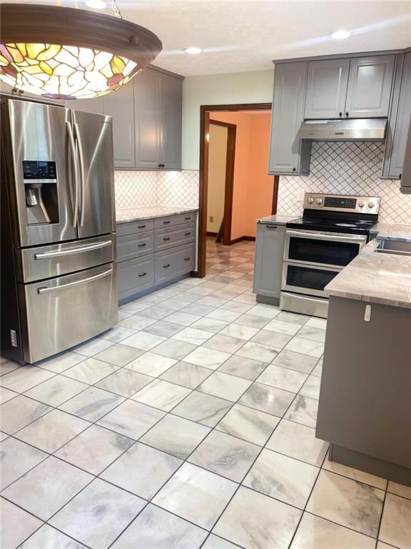 kitchen with light stone counters, stainless steel appliances, gray cabinets, and hanging light fixtures