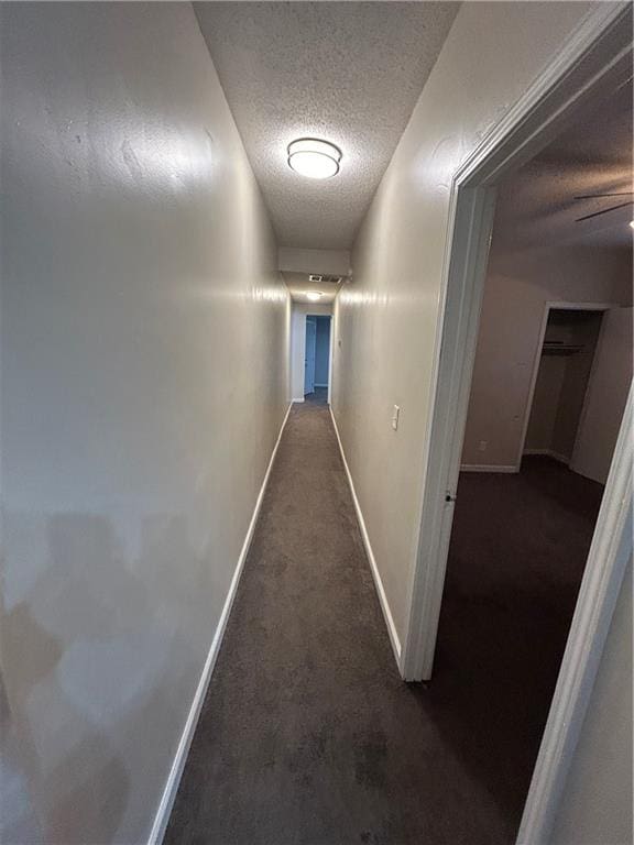 hallway featuring dark carpet and a textured ceiling