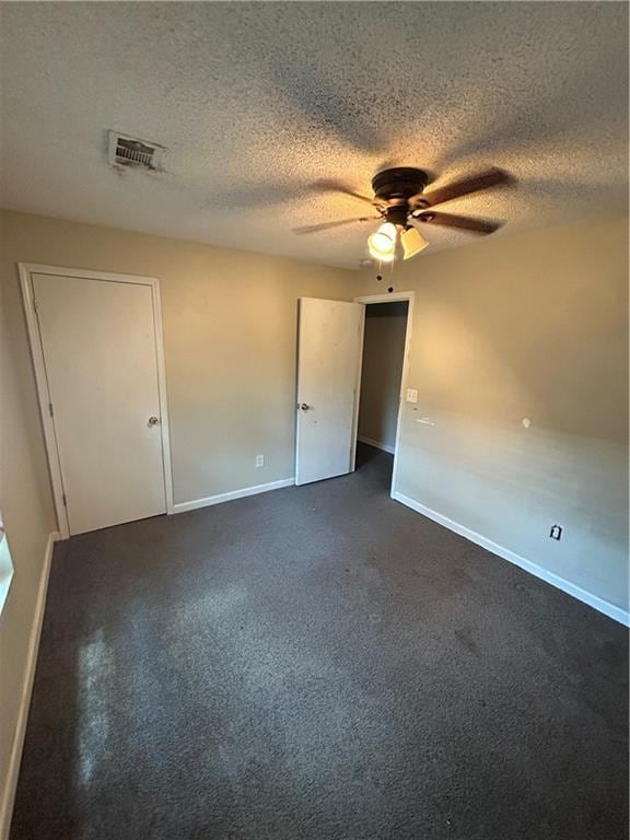 empty room featuring ceiling fan, a textured ceiling, and dark carpet