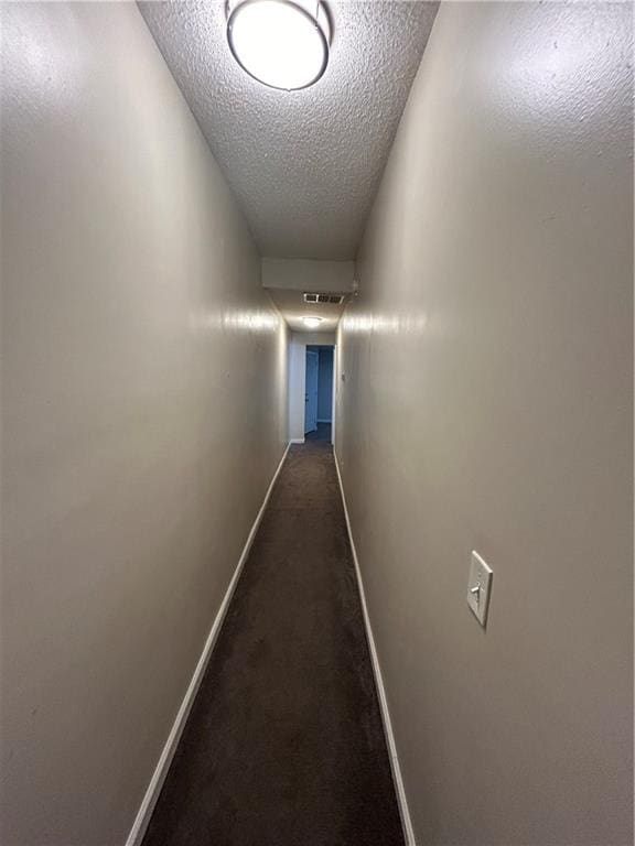 corridor with dark colored carpet and a textured ceiling