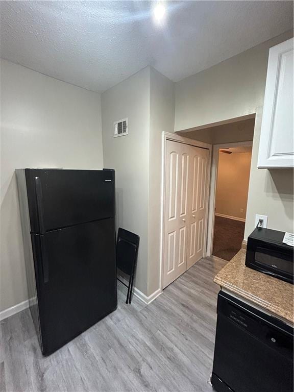 kitchen featuring white cabinetry, light hardwood / wood-style floors, black appliances, and a textured ceiling