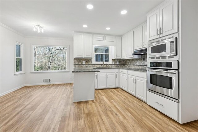 kitchen with white cabinets, dark stone countertops, light hardwood / wood-style floors, and tasteful backsplash