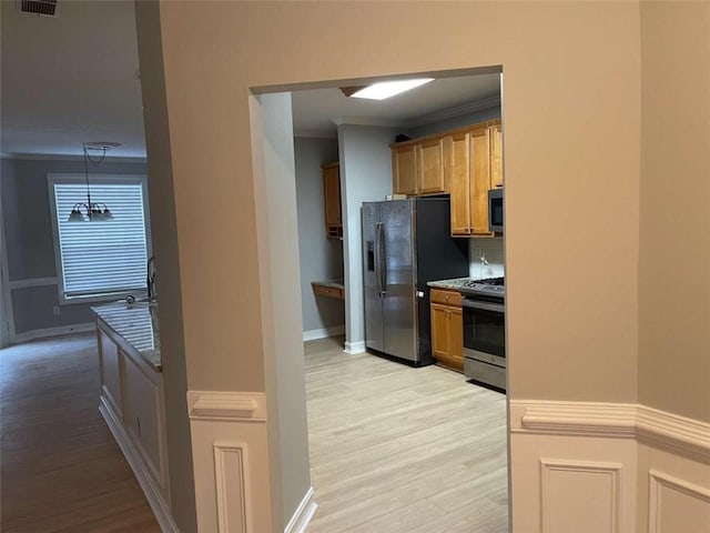 kitchen featuring a notable chandelier, crown molding, light hardwood / wood-style floors, appliances with stainless steel finishes, and pendant lighting