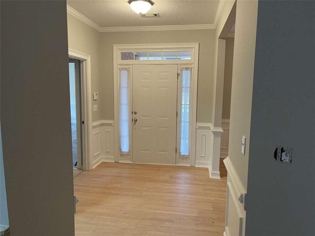 entryway with light hardwood / wood-style floors, a textured ceiling, and ornamental molding