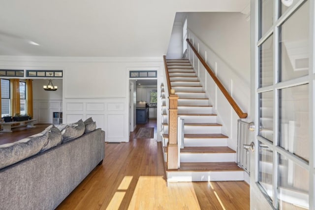 interior space featuring a decorative wall, stairway, light wood-style flooring, an inviting chandelier, and ornamental molding